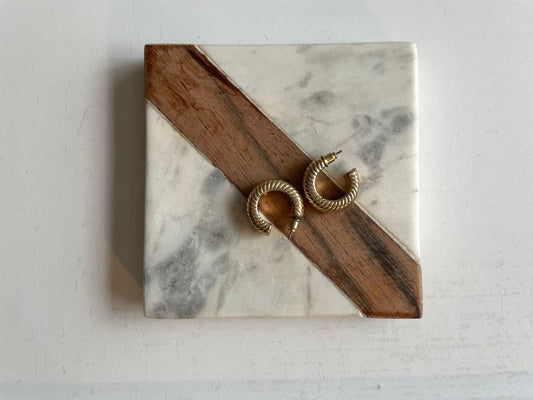 Gold hoop earrings resting on a marble bathroom counter beside folded towel