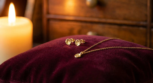 Gold vermeil stud earrings and delicate cable chain necklace on deep burgundy velvet with warm candlelight