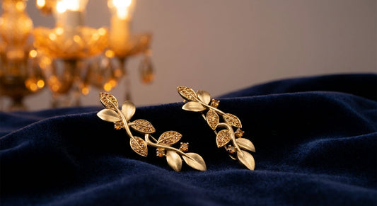 Gold ear climber jewelry resting against deep navy velvet fabric in warm amber chandelier lighting