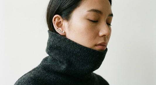Ear climbers visible against turtleneck collar fabric in natural light, editorial jewelry styling