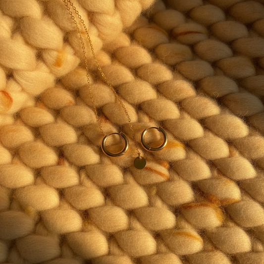 Gold hoop earrings and a fine gold necklace on a knit fabric in autumn daylight