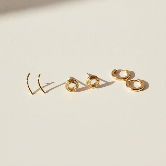 Three Juno & Fern earring styles flat lay — ear climbers, studs, and hoops — best earrings for a round face, gold vermeil on neutral background