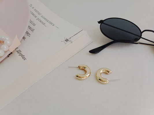 Gold stud earrings, small hoops and ear climbers arranged together on a neutral linen surface