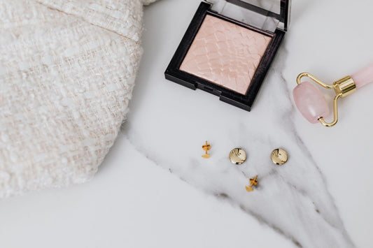 Gold stud earrings and a fine gold chain laid out on a neutral desk surface in daylight