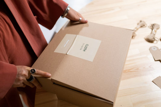 A small parcel and a folded jewelry pouch on a pale wooden table in soft daylight